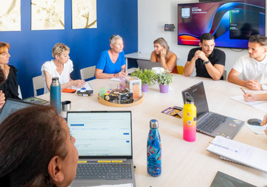 Réunion d'équipe en salle bleue, collaborateurs avec ordinateurs portables et écran d'affichage