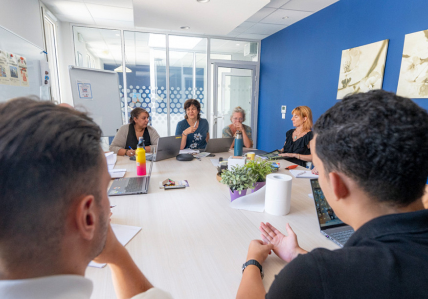 Réunion d'équipe autour d'une table, mur bleu, collaborateurs avec ordinateurs portables
